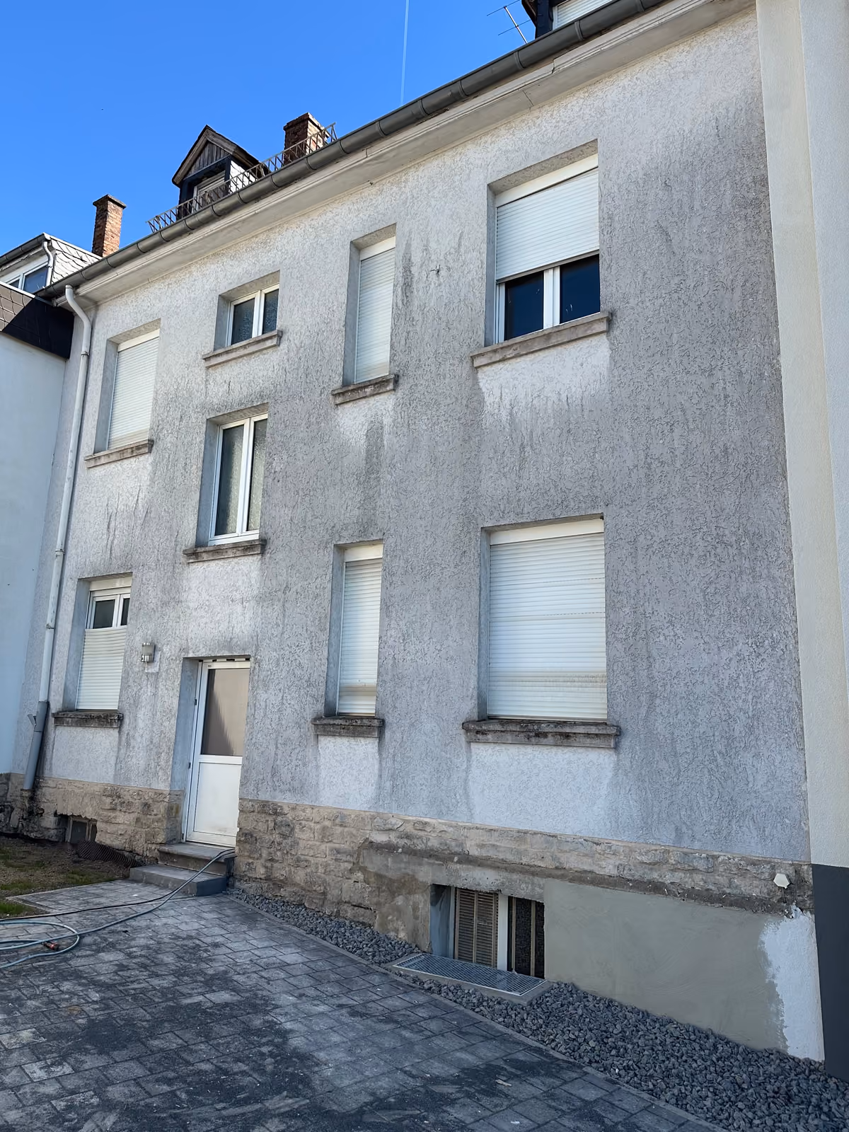 Veralgte und verschmutzte Mehrfamilienhaus-Fassade mit Schmutzstreifen vor der Reinigung