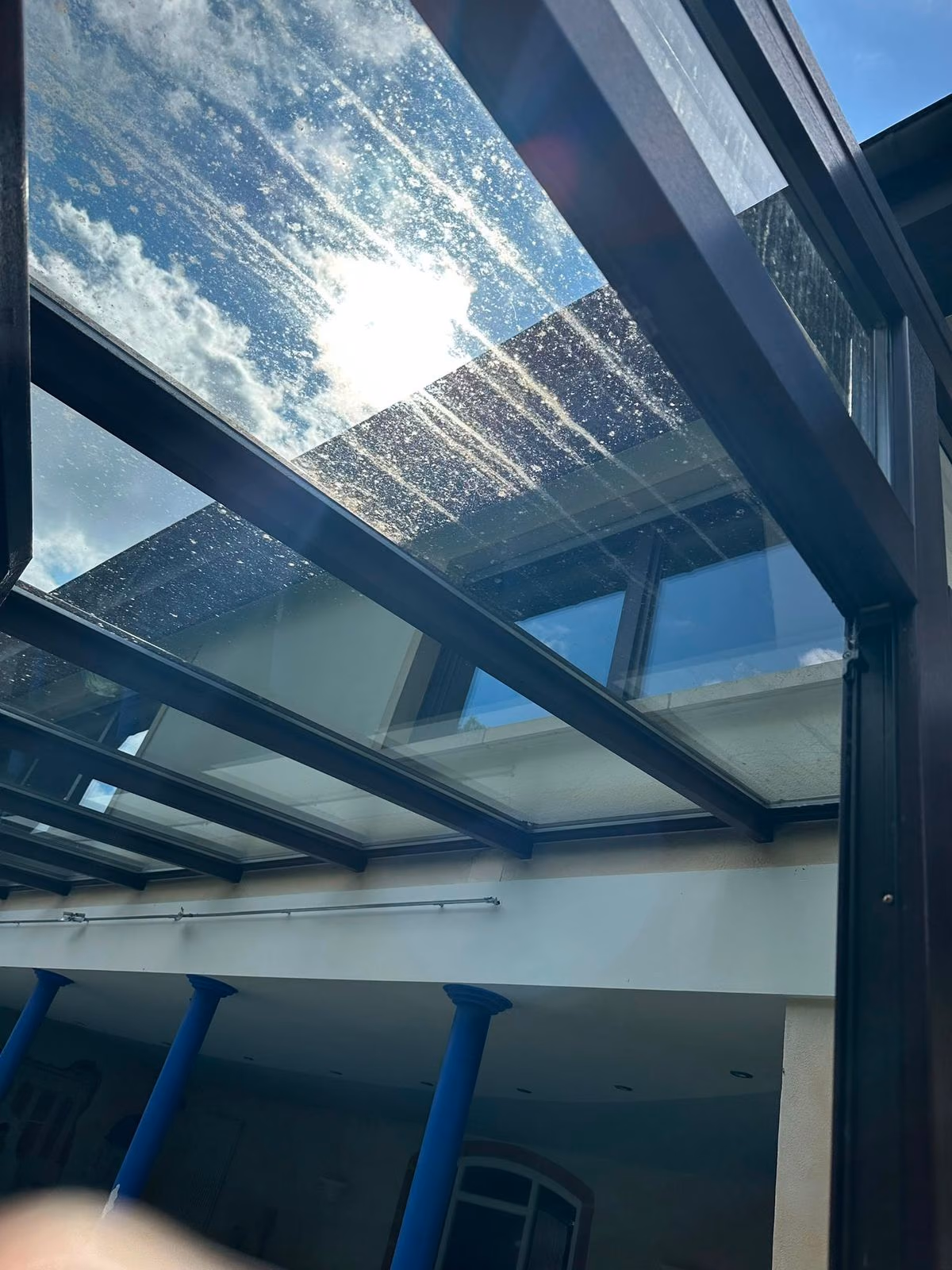 Dirty glass roof of a patio cover with water stains before cleaning